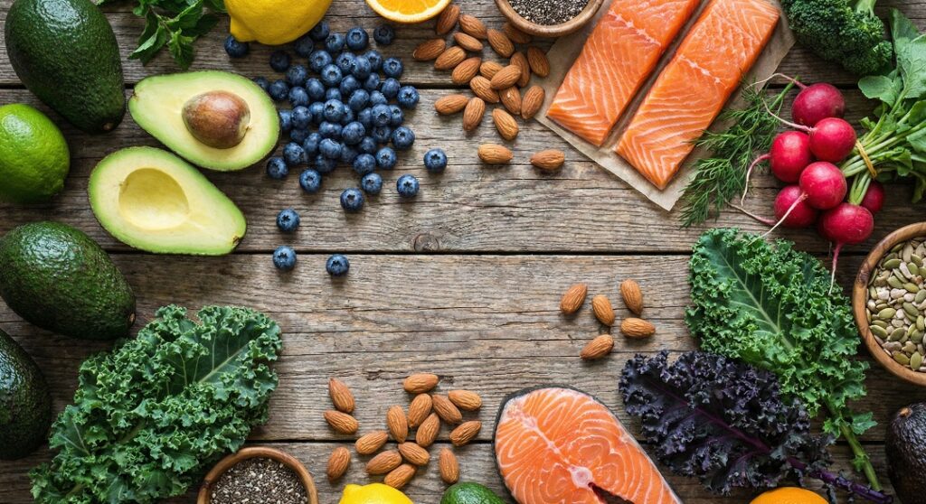 A colorful assortment of super healthy foods including salmon, avocados, nuts, and berries on a wooden table.